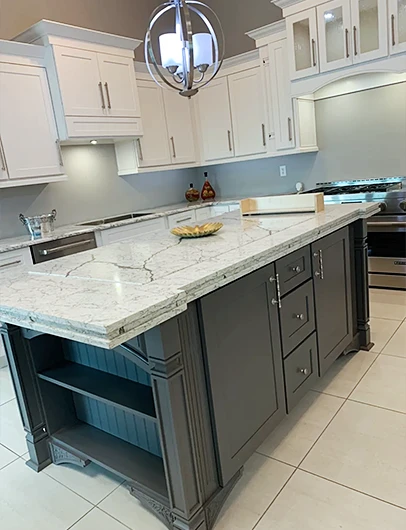 A kitchen with a large two-toned island with a gray base and a white marble-patterned countertop, and white surrounding cabinets.