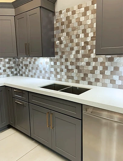 A modern kitchen with dark gray cabinets, white countertops, and a unique mosaic tile backsplash.