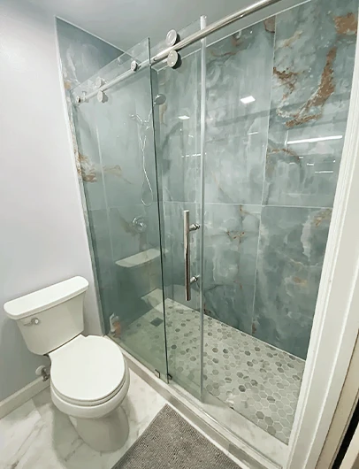 A modern bathroom with a walk-in shower that has a sliding glass door, a mosaic tile floor, and unique blue and gold marble-patterned walls.