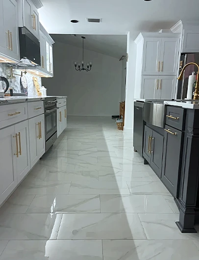 A modern galley kitchen with white and dark two-toned cabinets, gold hardware, and marble-patterned floors.
