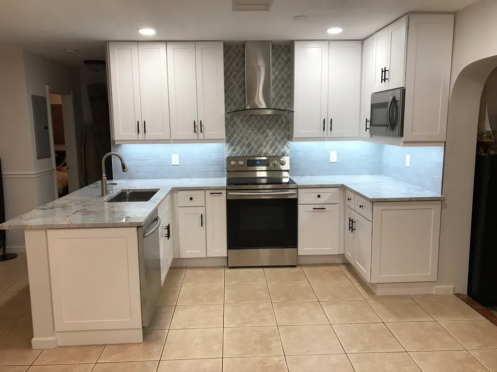 A modern U-shaped kitchen with white cabinets, stainless steel appliances, and a two-toned backsplash with blue subway tiles and a gray mosaic pattern.