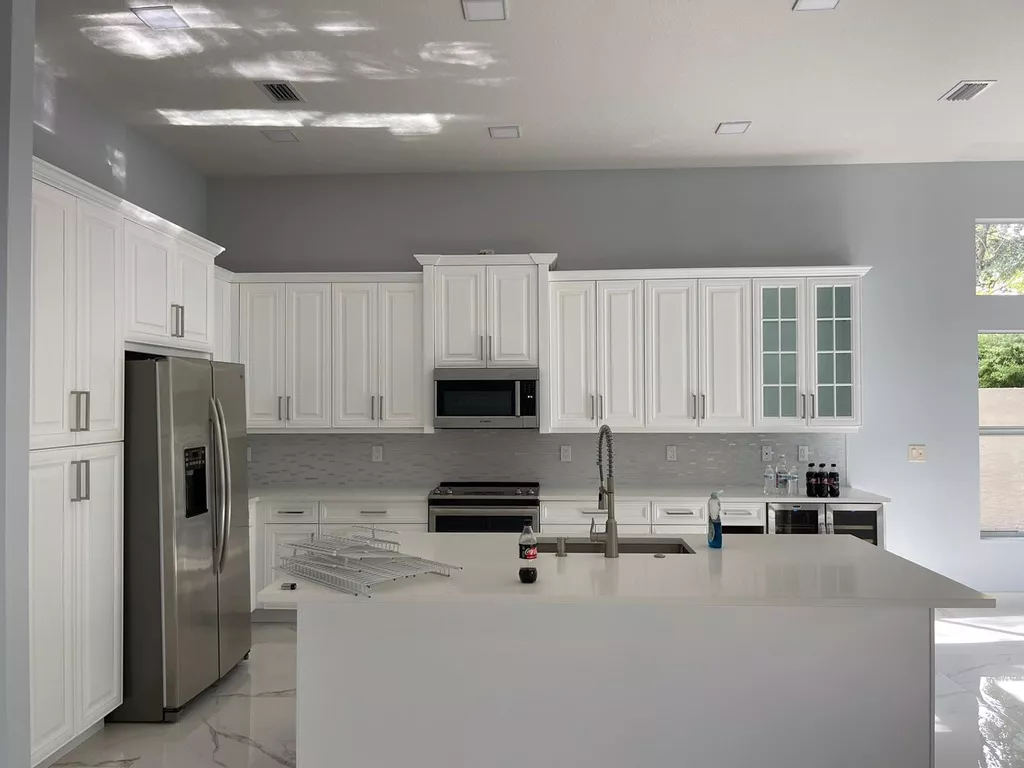 A modern kitchen with a large white island, white cabinets, stainless steel appliances, and gray walls.