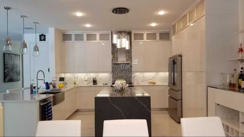 A modern kitchen with glossy white cabinets, a central black marble-patterned island, and stainless steel appliances.