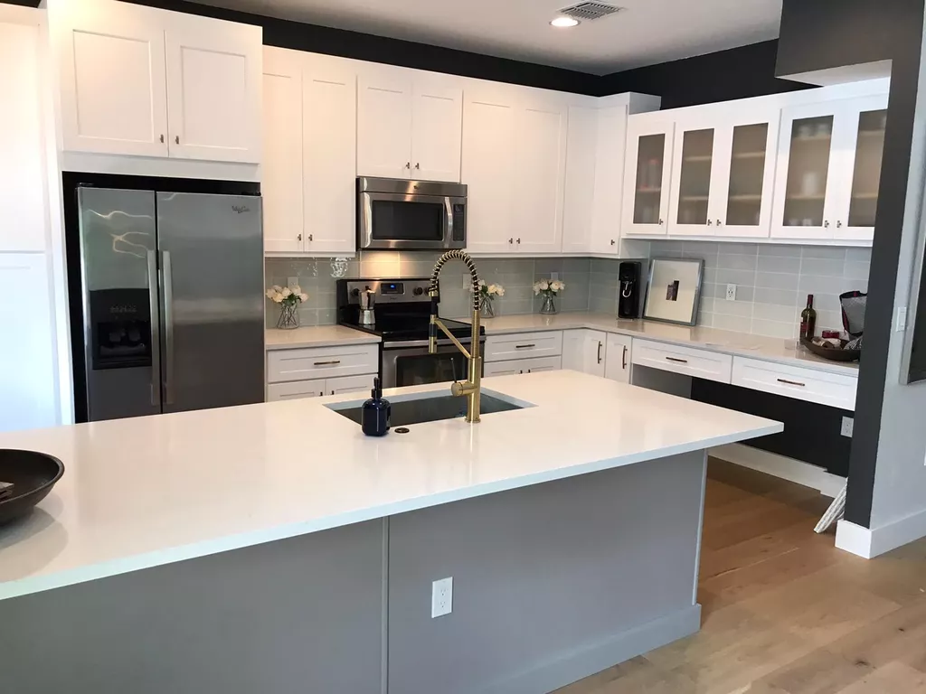A modern kitchen with a two-toned gray island, a gold faucet, white cabinets, and a black accent wall.