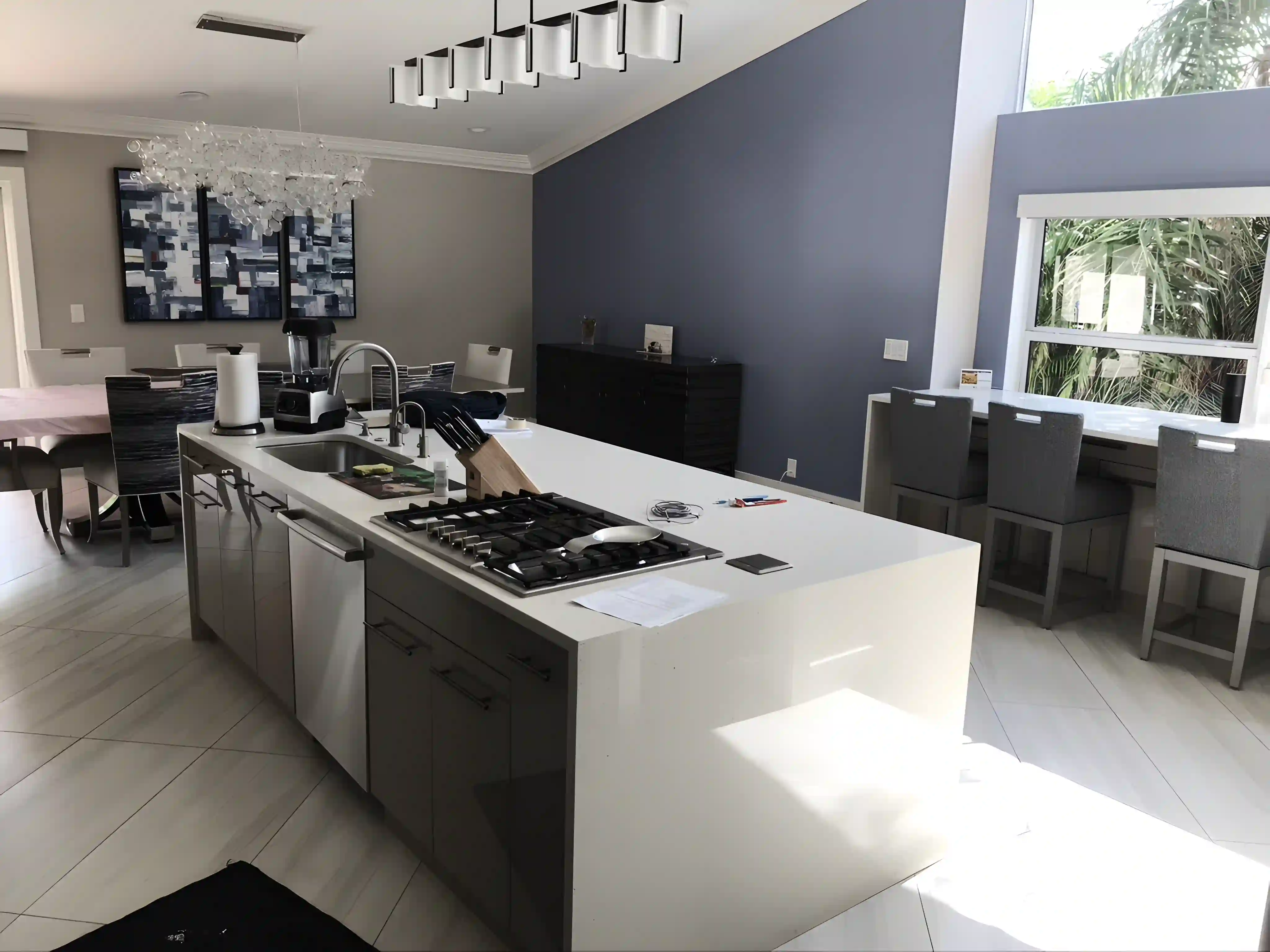 A modern kitchen with a large white island, gray accent wall, and large windows.