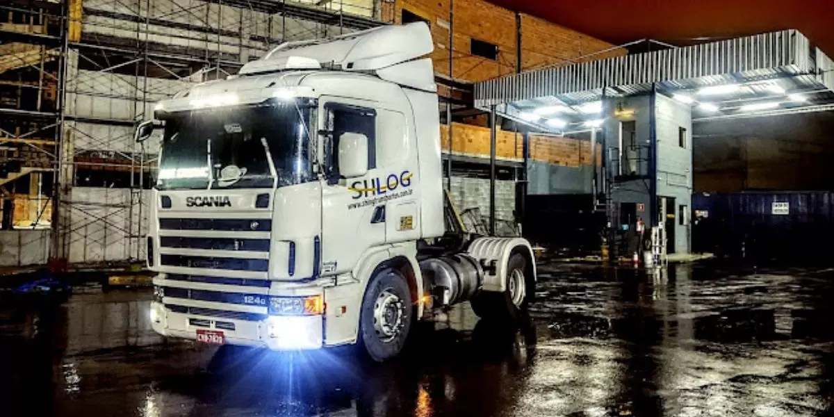 A foto mostra um caminhão branco da SHLOG