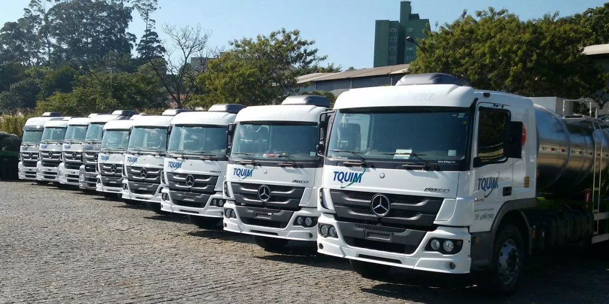 A foto mostra uma frota de caminhões da TQUIM Transportes