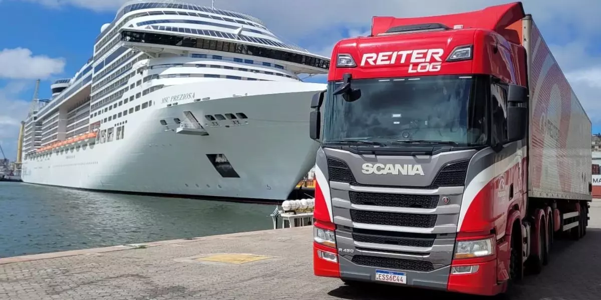 A foto mostra uma carreta da Reiter Log e um navio