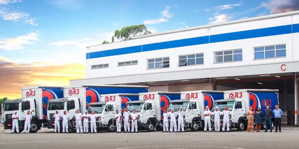 A foto mostra uma frota de caminhões e motoristas da R3 Transportes