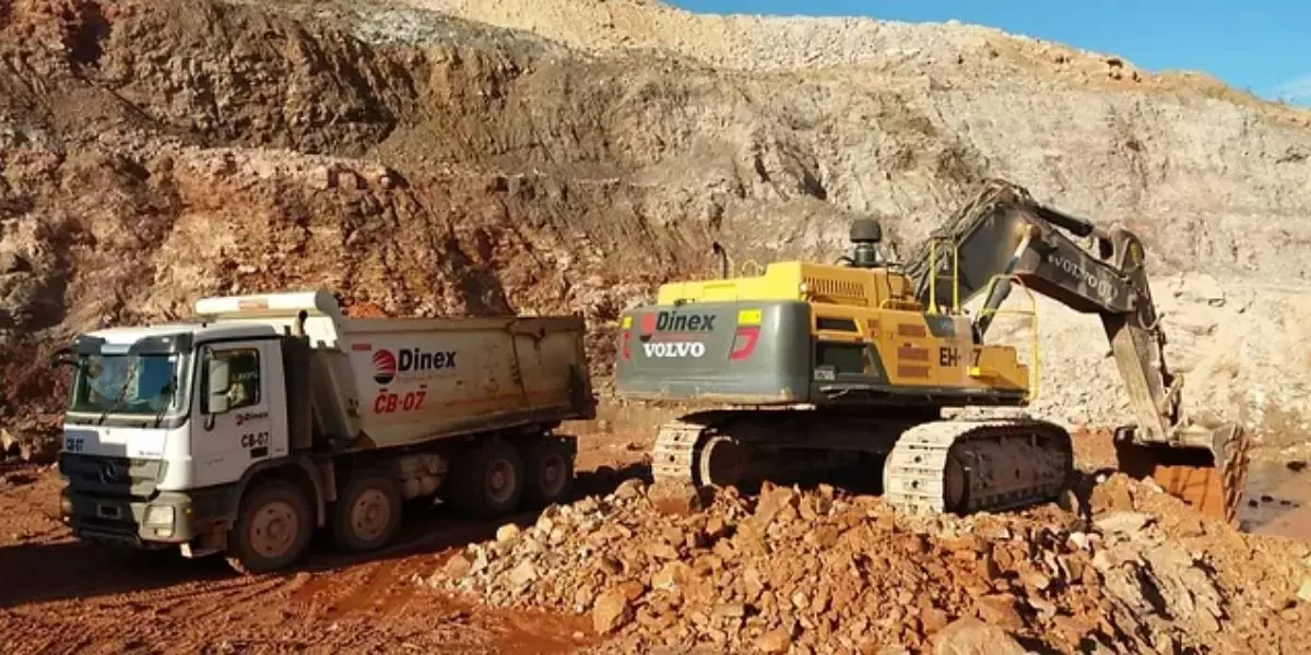 A foto mostra um caminhão basculante e uma escavadeira hidráulica da Dinex Engenharia
