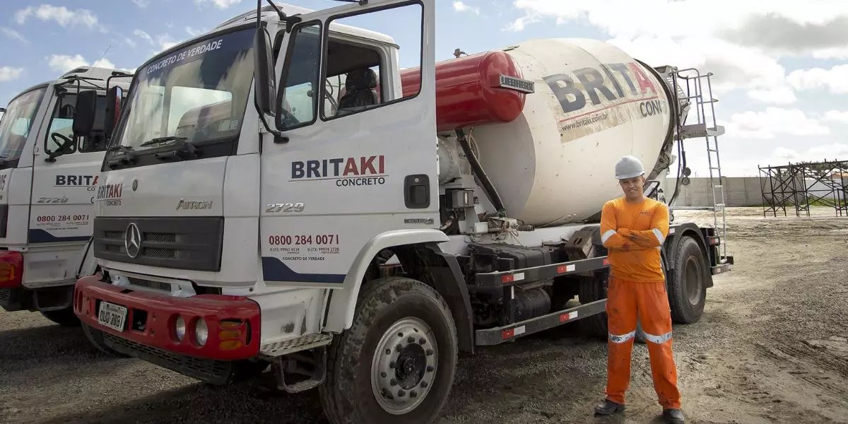A foto mostra dois caminhões e um motorista da Britaki Concreto