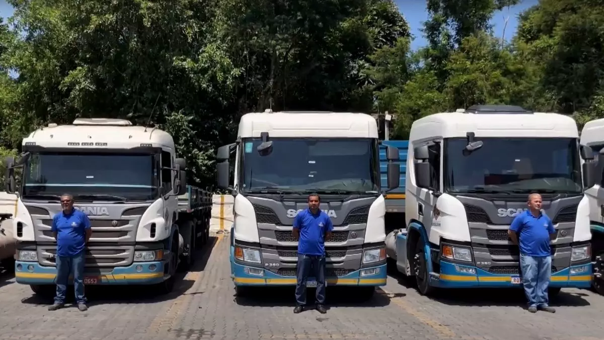 A foto mostra uma frota de caminhões e motoristas da Transportes Excelsior