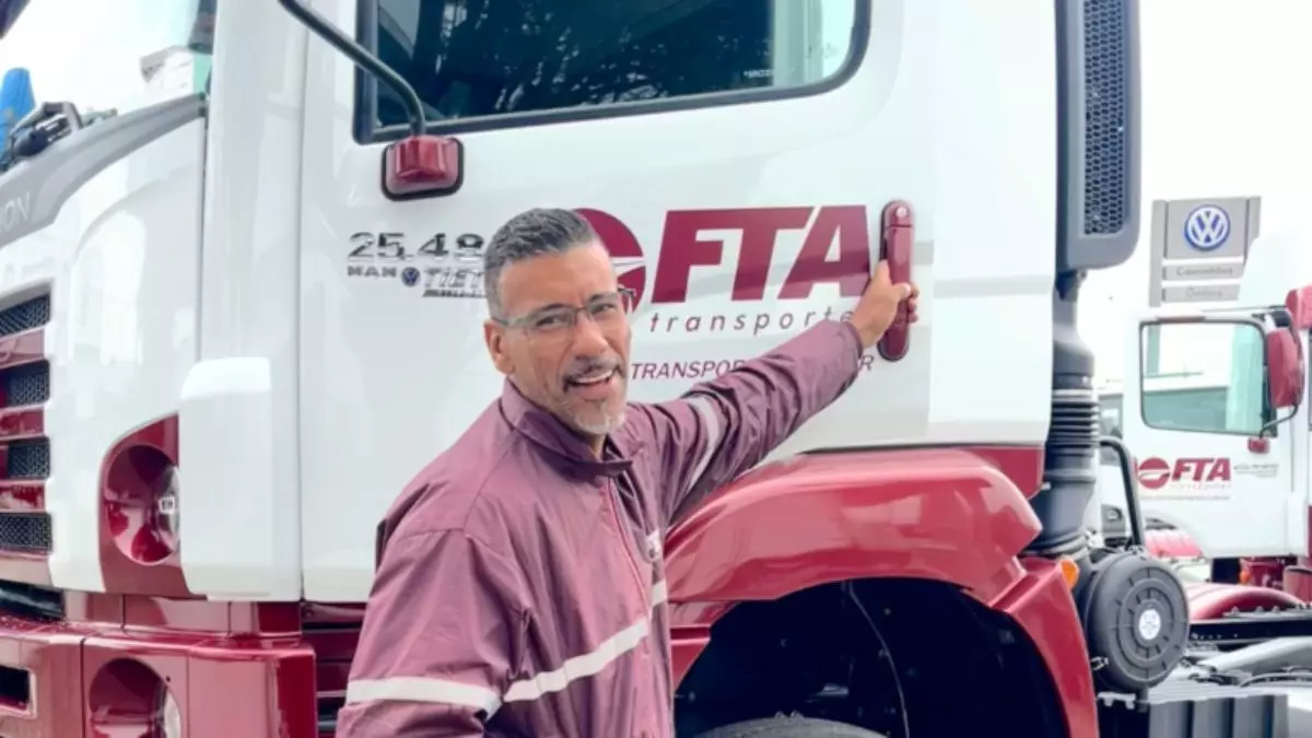 A foto mostra um motorista entrando em um caminhão da FTA Transportes
