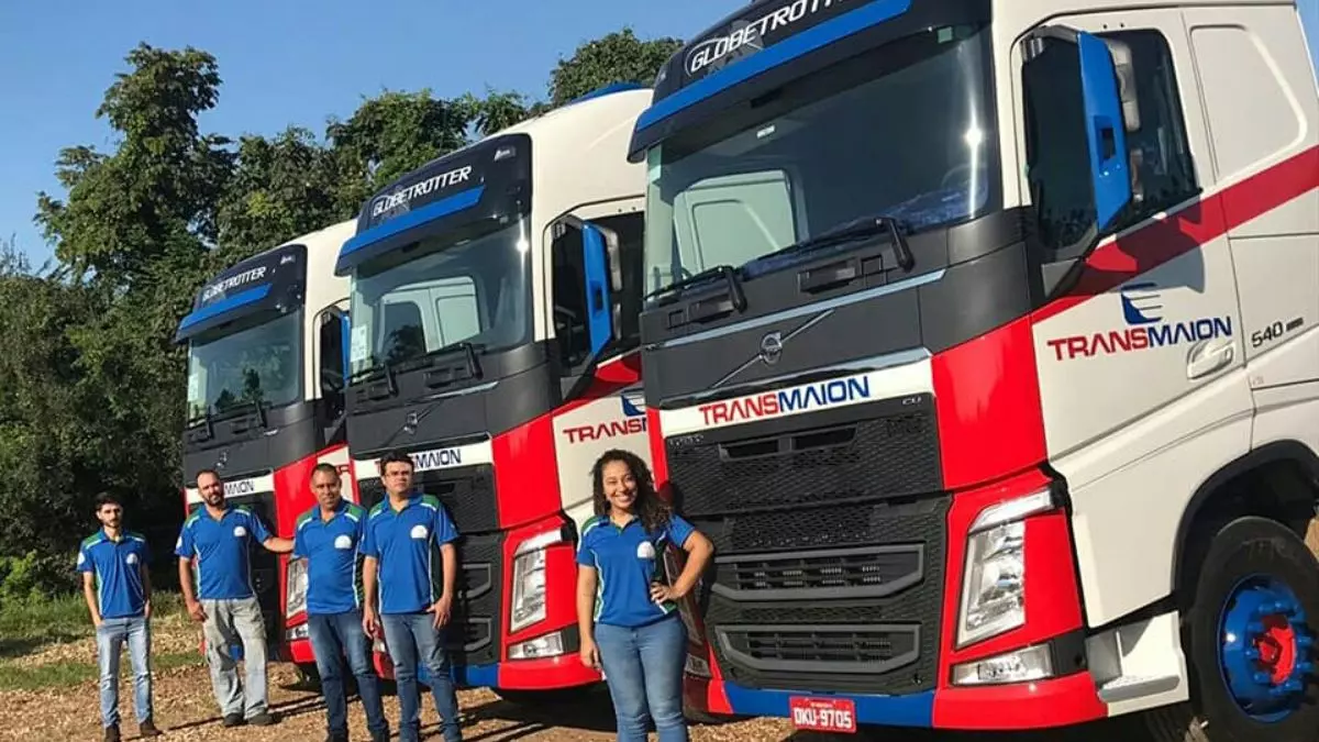 A foto mostra uma frota de caminhões e vários motoristas da Transmaion